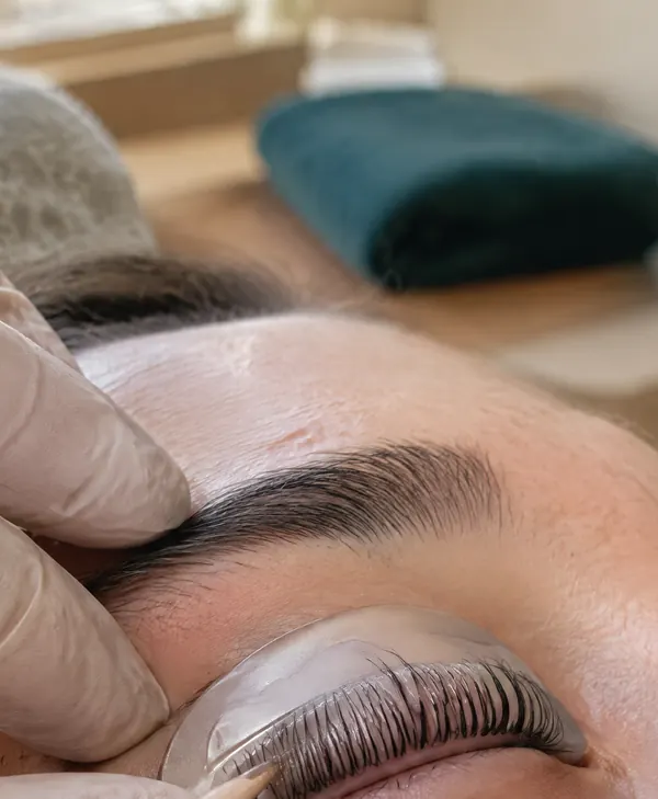 Geliftete Wimpern auf dem Silikonpad, eine Hand führt das Holzstäbchen